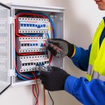 Electrician wearing safety gloves working inside open circuit breaker panel