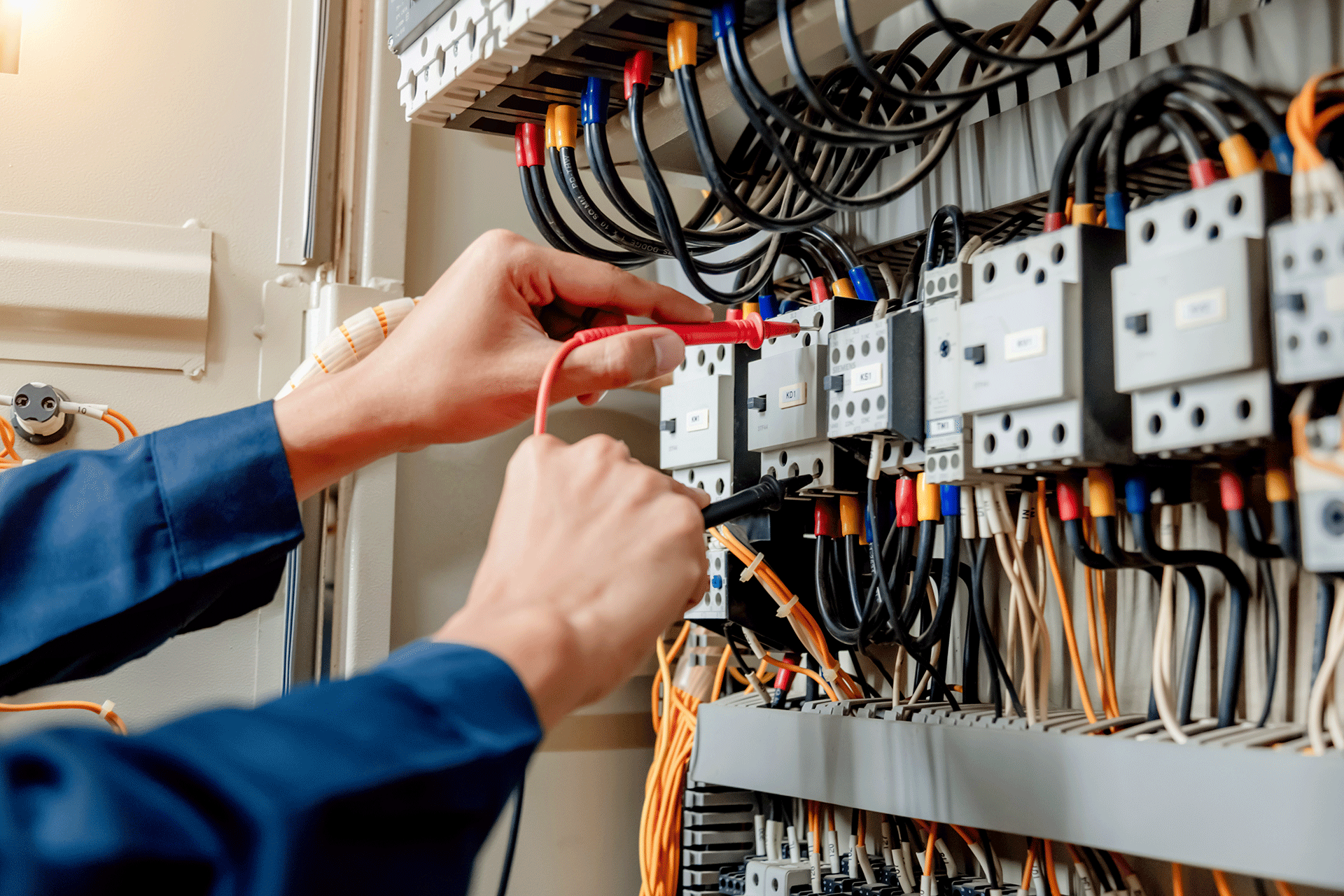 Electrician testing wiring and electrical components in a distribution panel using a multimeter.